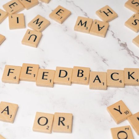 Wooden Scrabble tiles arranged to spell 'Feedback' on a marble background.